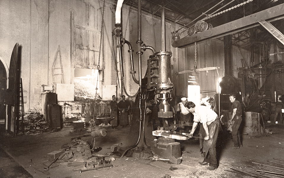 Blacksmith forging a locomotive foundation bar on a steam hammer in the Blacksmith Shop. Blacksmith forging a locomotive foundation bar on a steam hammer in the Blacksmith Shop.